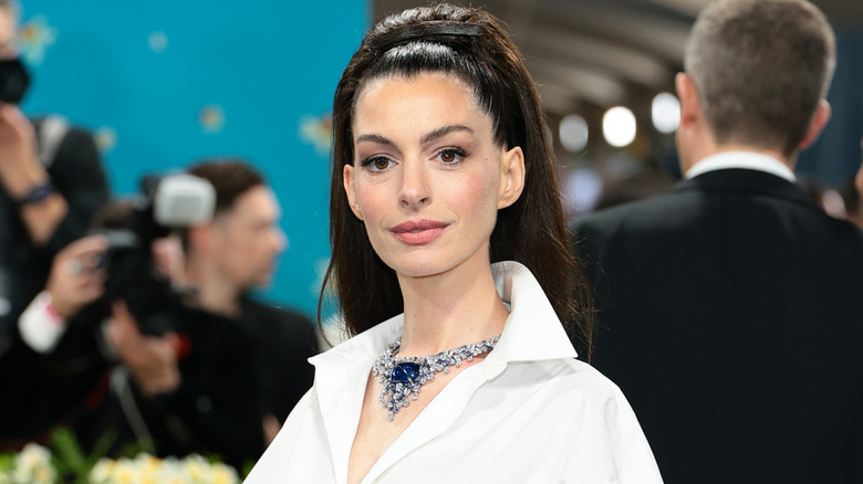 Anne Hathaway with a sleeked back ponytail, white shirt, and Bulgari necklace