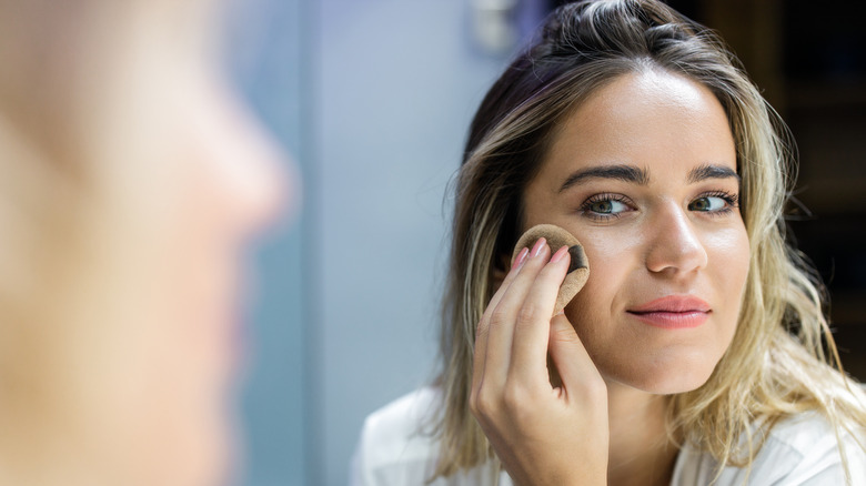 woman applying powder in mirror