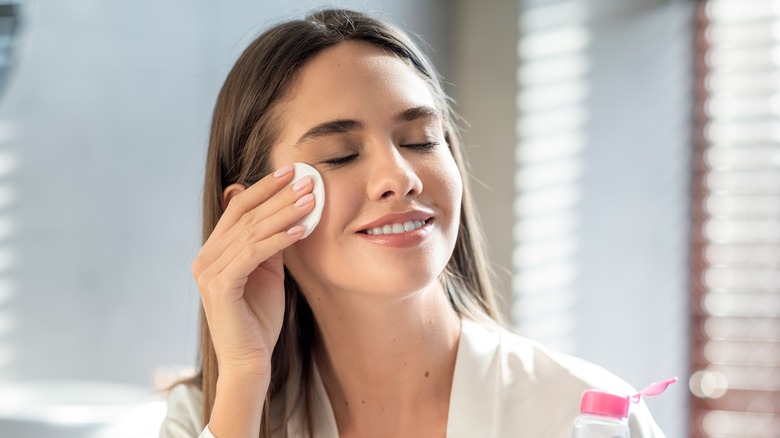 smiling woman applying toner to her face 