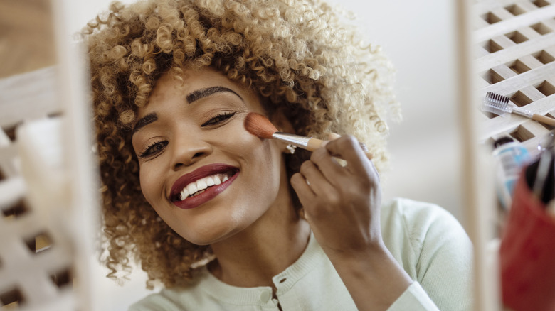 Woman applying blush to cheeks