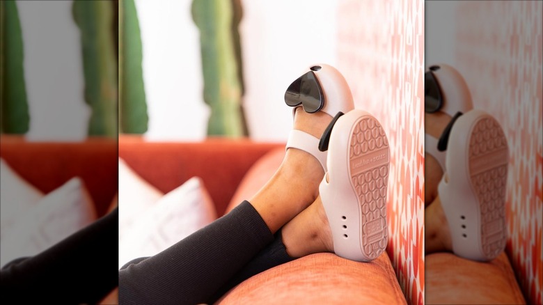 A child wearing a pink pair of Baubles + Soles shoes with black heart attachments