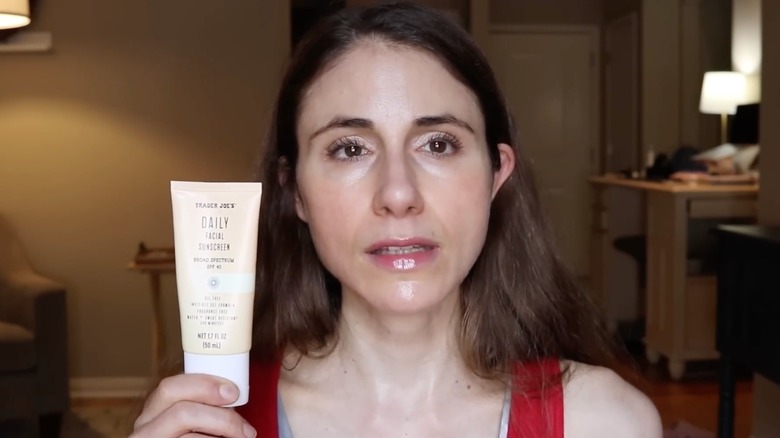 A doctor holding up a tube of the Trader Joe's Daily Facial Sunscreen while filming a video