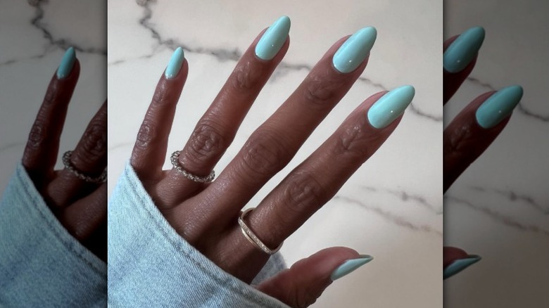 A bright blue manicure on a hand with rings