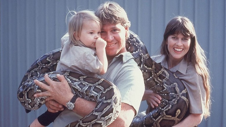 Bindi Irwin as a baby being held by Steve Irwin, who is also holding a giant snake next to Terri Irwin