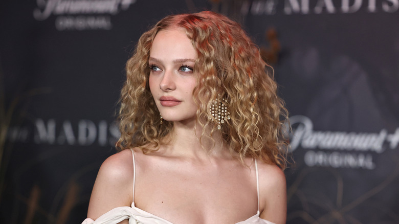 The Madison star Amiah Miller wearing a white off-the-shoulder dress and earrings on a red carpet