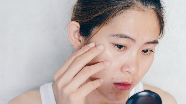 woman examining face in mirror