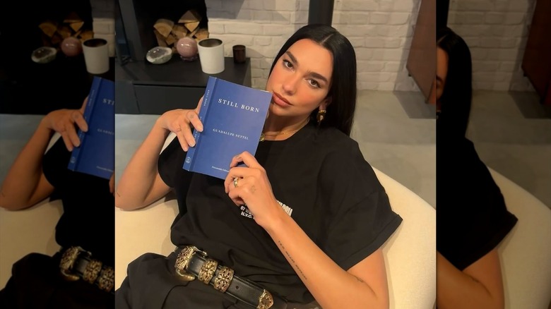 Dua Lipa holding up the book "Still Born"