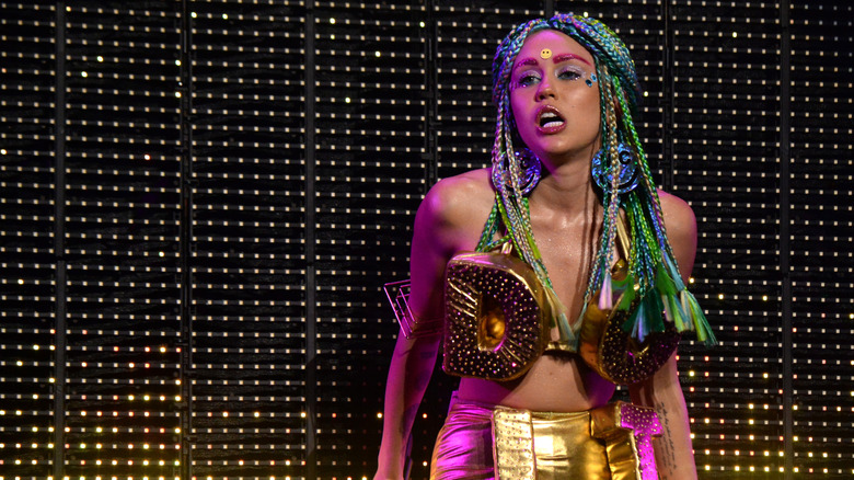 Miley Cyrus in a rainbow braided wig and gold two piece