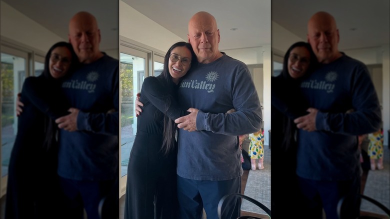 Demi Moore wearing glasses and a black outfit hugging Bruce Willis wearing a blue sweatshirt.