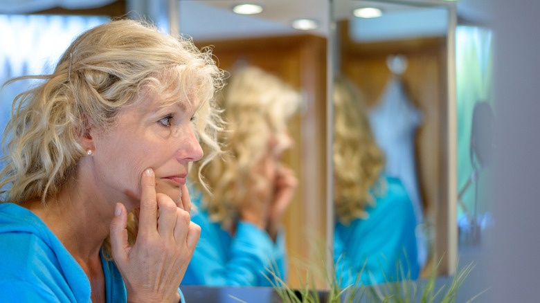 Woman pulls on cheeks in mirror