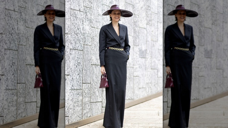A woman wearing a large hat and pinstripe black outfit