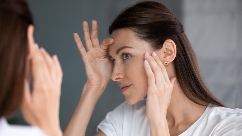 woman examining wrinkles in mirror