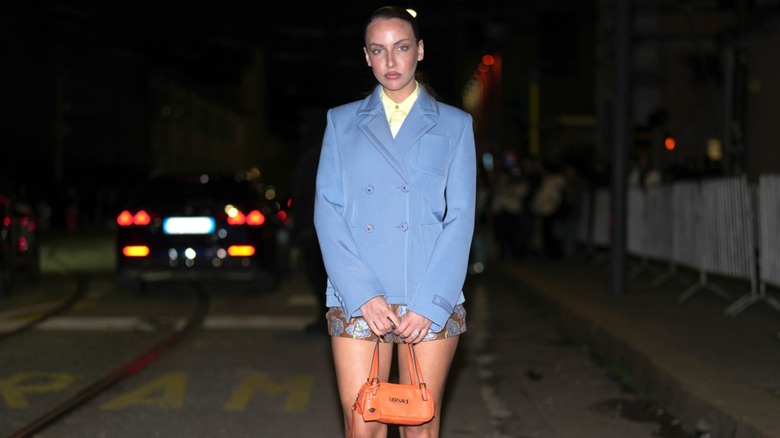 A model wearing a light-blue blazer and carrying an orange handbag