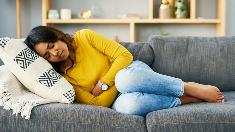 Woman holding abdomen on sofa