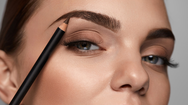 Person creating thick eyebrows with a brown pencil