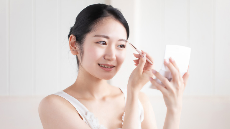 Woman drawing her eyebrows while looking in a mirror