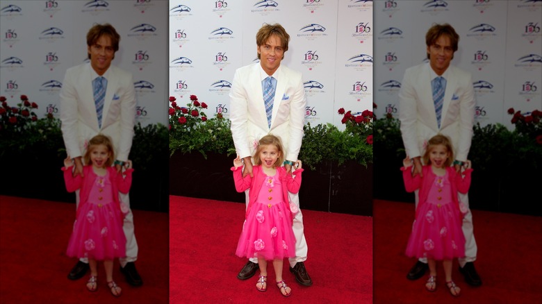 Dannielynn Birkhead smiles in front of Larry Birkhead wearing a hot pink dress