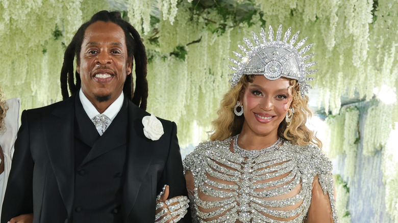 Jay-Z in a black suit and Beyoncé wearing an ornate crystal outfit posing together at an event.