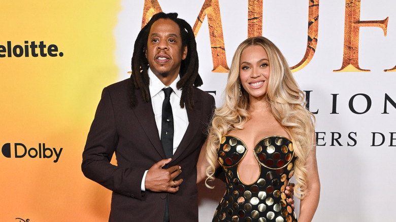 Jay-Z in a suit and Beyoncé in a strapless dress with large gold sequins posing at a red carpet event.