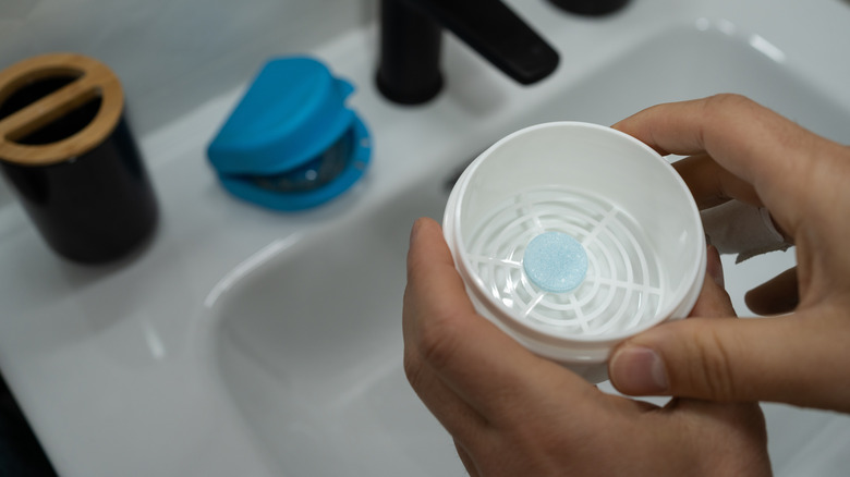Hands holding pot containing denture tablet