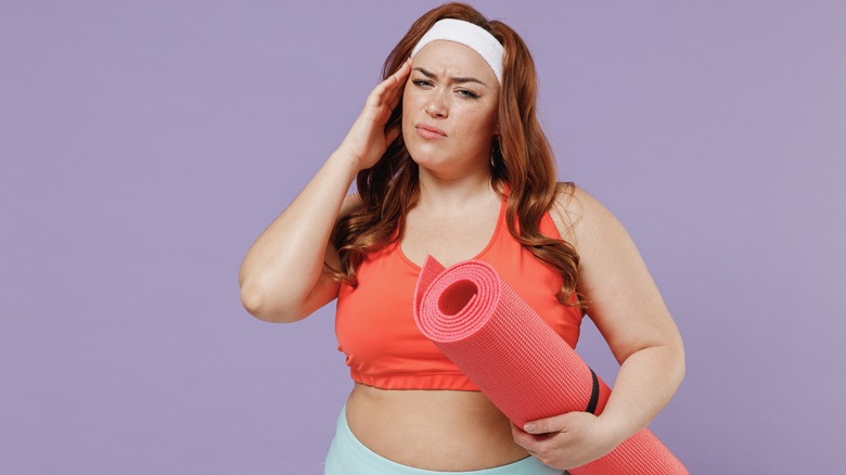 woman with headache holding yoga mat