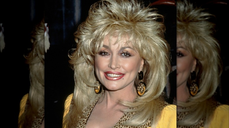Dolly Parton with feathered hair in a yellow outfit