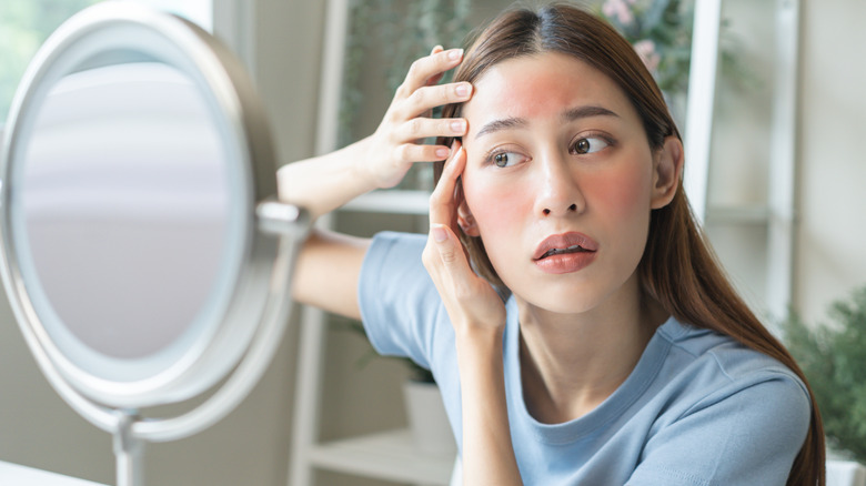 A woman examining her red face in a beauty mirror