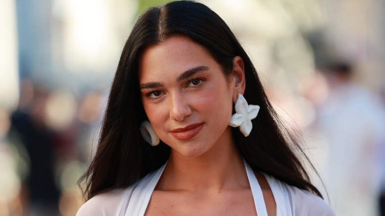 Dua Lipa poses for photos at a wedding while wearing white earrings