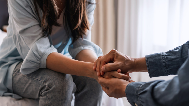 One person comforting another, holding hands