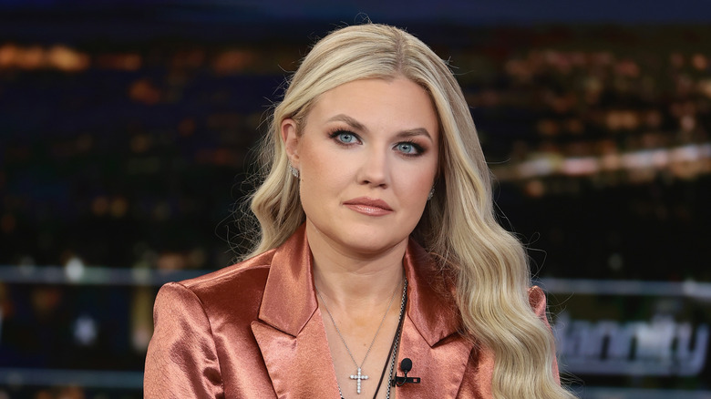 Erika Kirk sitting silently while wearing a poorly-fitted copper blazer