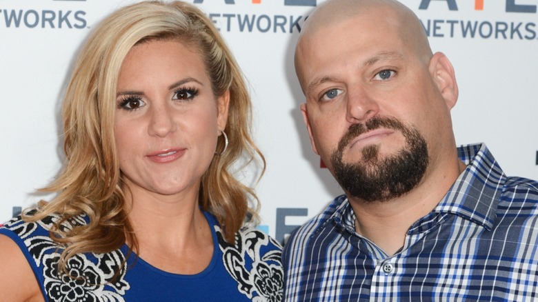 Brandi Passante and Jarrod Schulz. Jarrod is a white man with a bald head and dark facial hair. He is wearing a blue plaid button down shirt. Brandi is wearing a blue, white, and black sleeveless blouse and silver hoop earrings.