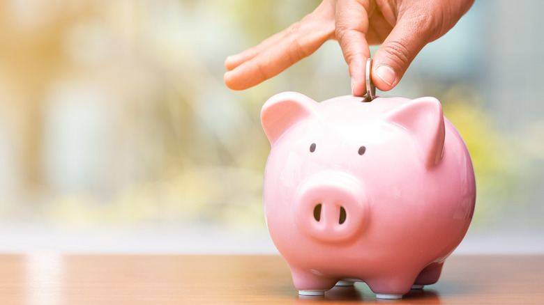 A hand putting coins in a piggy bank