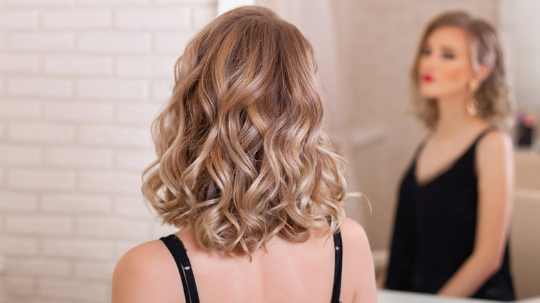 woman with short curly blonde hair looking in mirror