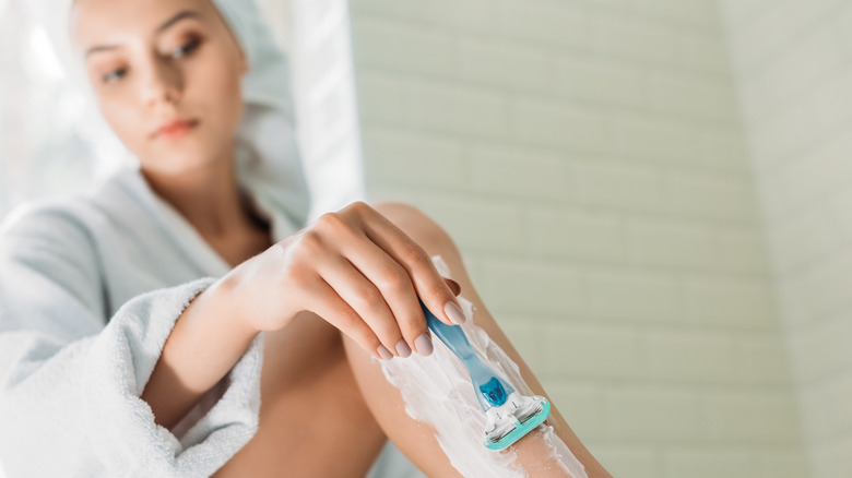 Woman shaving legs bathrobe