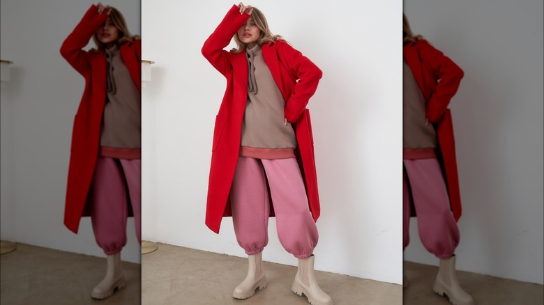 A woman layers a long red coat over a sweatshirt and sweatpants