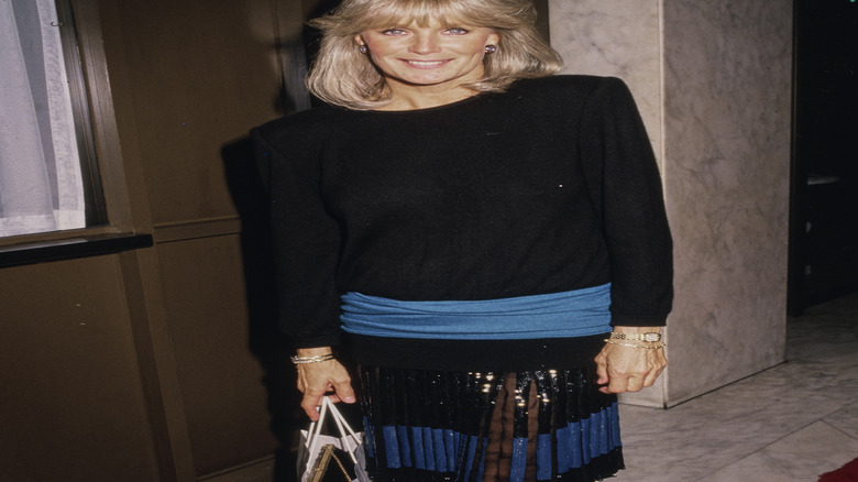 A woman wearing a black garment with large shoulder pads