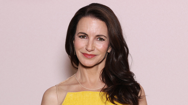 Kristin Davis wears a bright yellow dress and a bold red lip while posing in front of a light pink background
