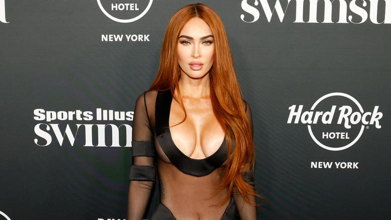 Megan Fox wears a plunging, sheer black gown and has red hair parted down the middle