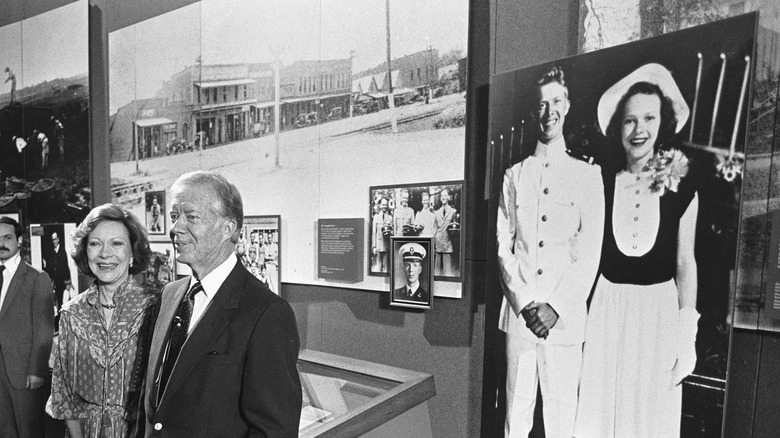 Jimmy Carter and Rosalynn Carter stand in front of their wedding photo in a museum