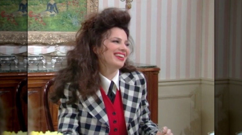Fran Fine laughs at the breakfast table while wearing a red vest, black and white plaid blazer, white collar, and black tie