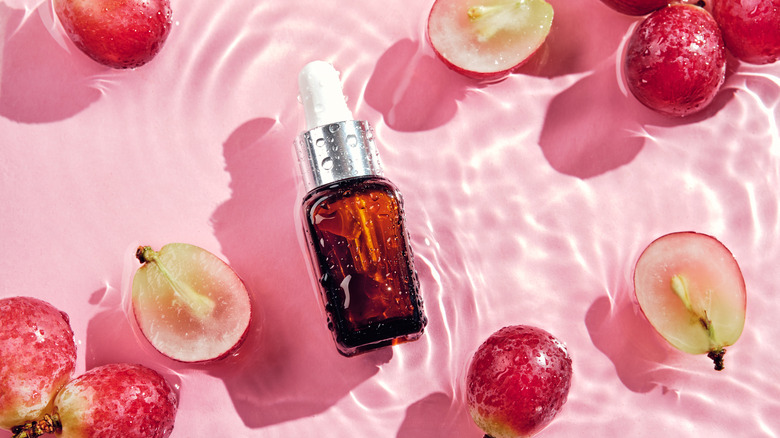 Small bottle and grapes against pink background