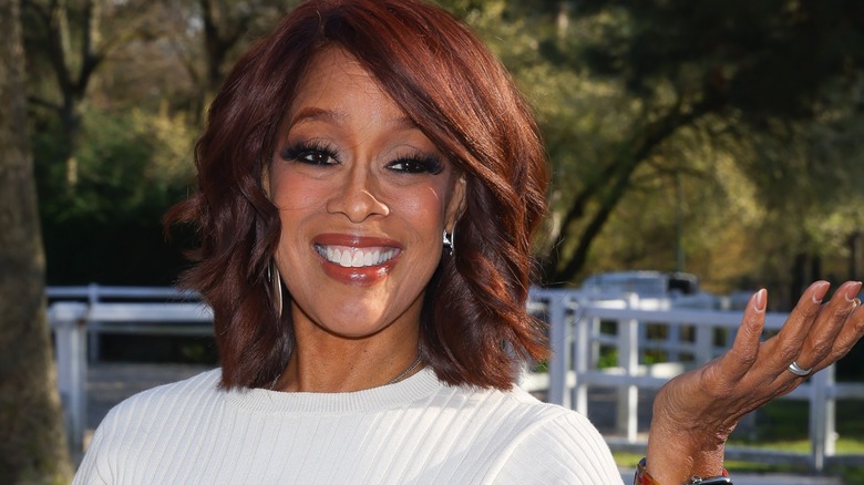 A close-up image of Gayle King smiling and posing with her hand out