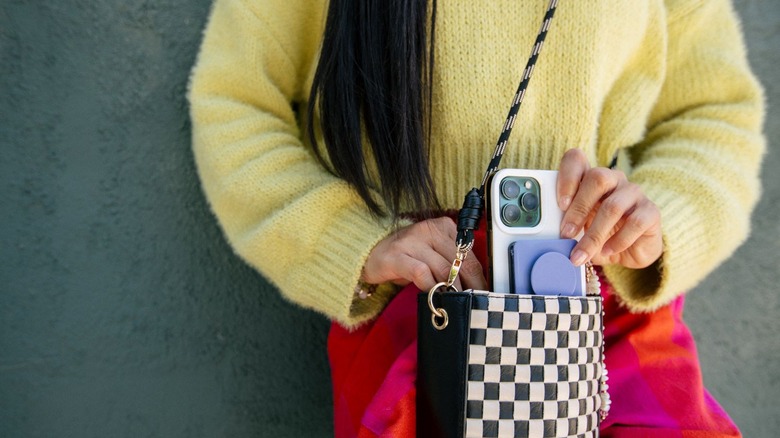 Person wearing yellow sweater removing a phone from a black and white checkered purse