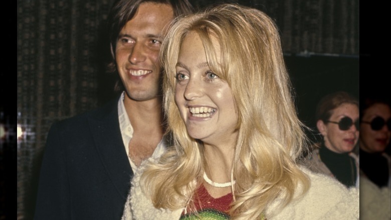 Goldie Hawn smiling with no makeup wearing a white sweater and white necklace.