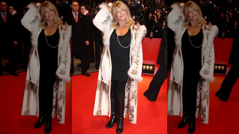 Goldie Hawn at a red carpet event wearing an all-black outfit and a long silky coat with a fur trim.