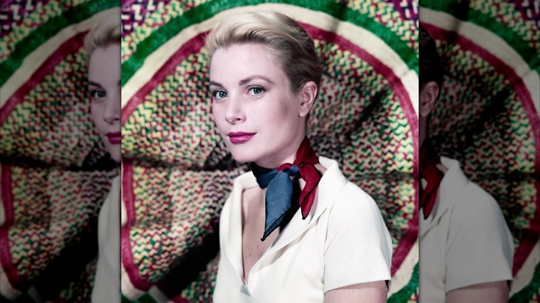 Grace Kelly with her hair up wearing a white shirt and a blue and red scarf in front of a colorful background.