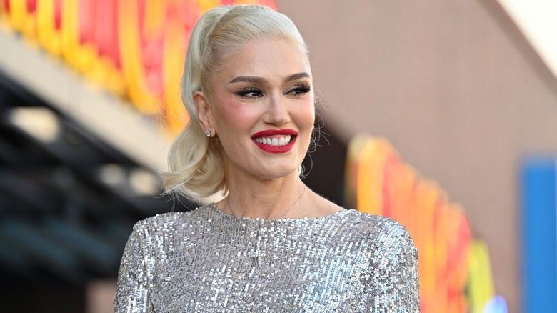 Gwen Stefani smiling with red lips and her blond hair up in a ponytail