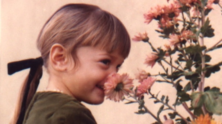 A young Gwen Stefani with naturally brown hair in a ponytail smelling flowers
