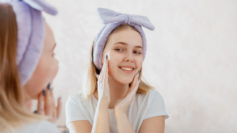 young woman washing face looking at mirror