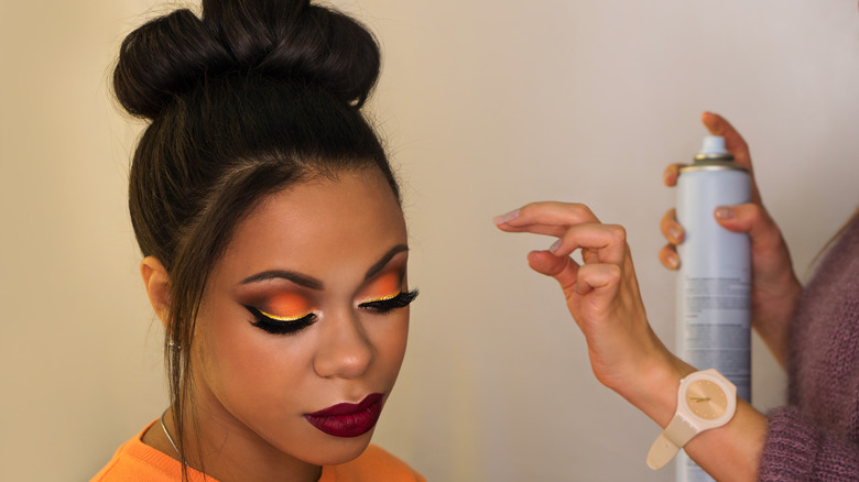 stylist spraying hairspray on woman's hair